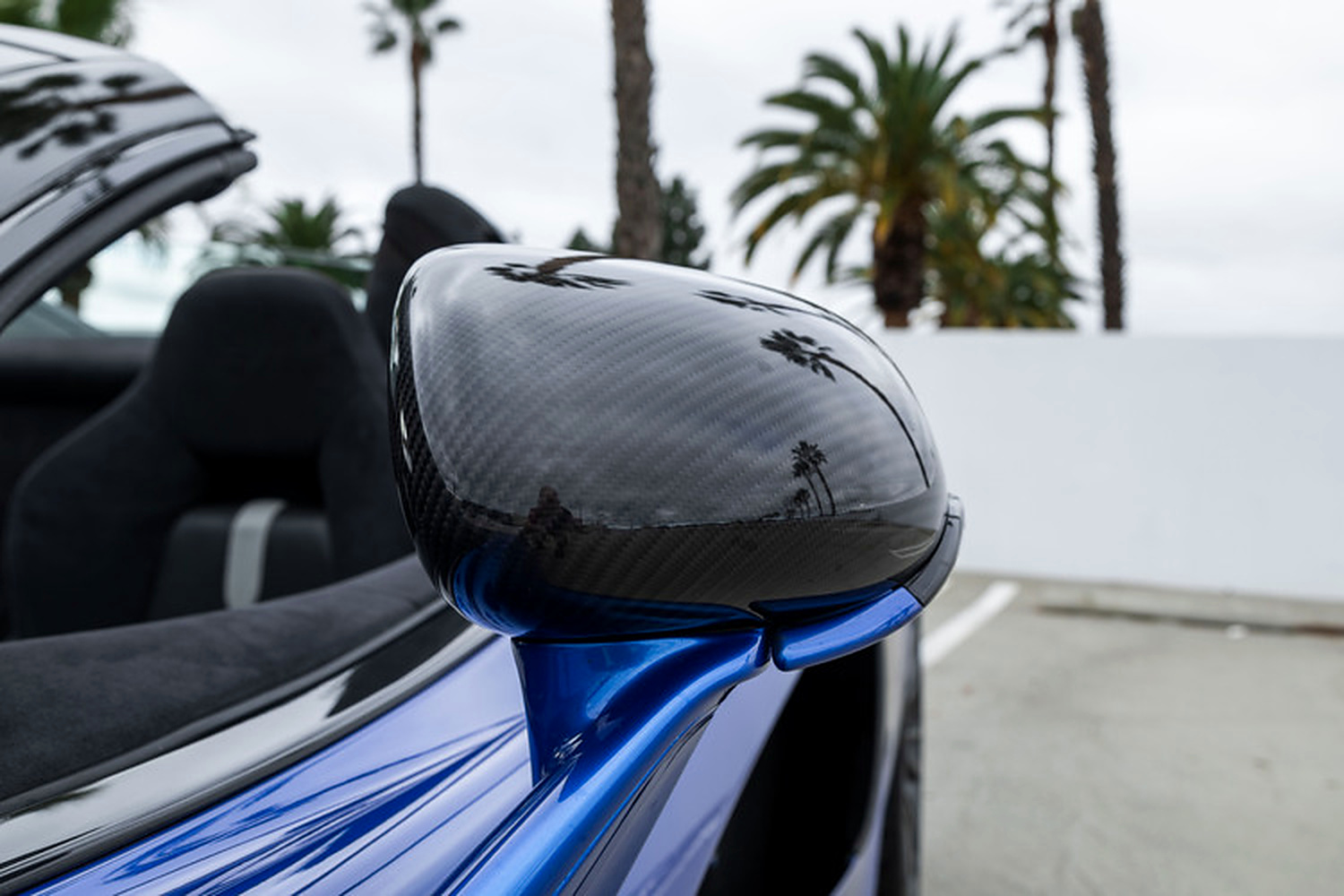 Carbon fibre mirror casing on the blue McLaren 570S Spider with palm trees behind