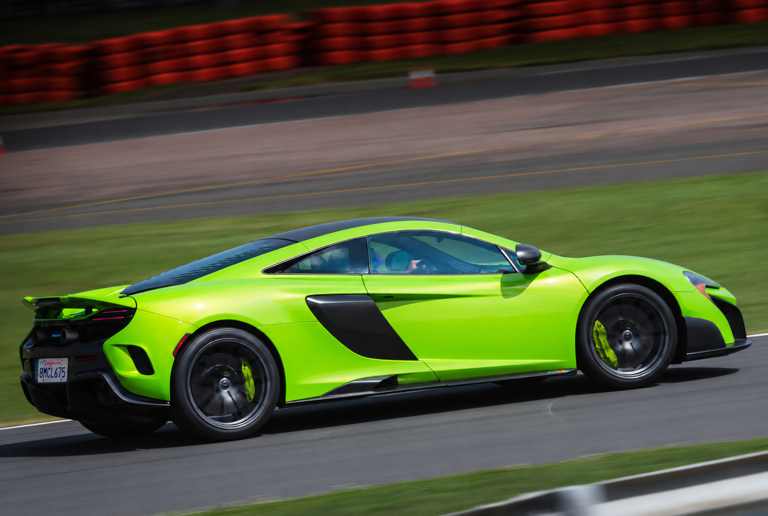 Green McLaren 675LT in motion on a race circuit with red and white kerbs blurred behind