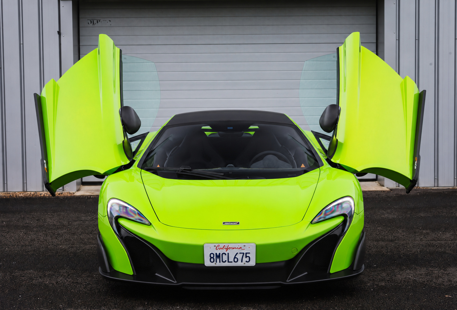 Head-on view of the green McLaren 675LT with both dihedral doors raised outside a hangar