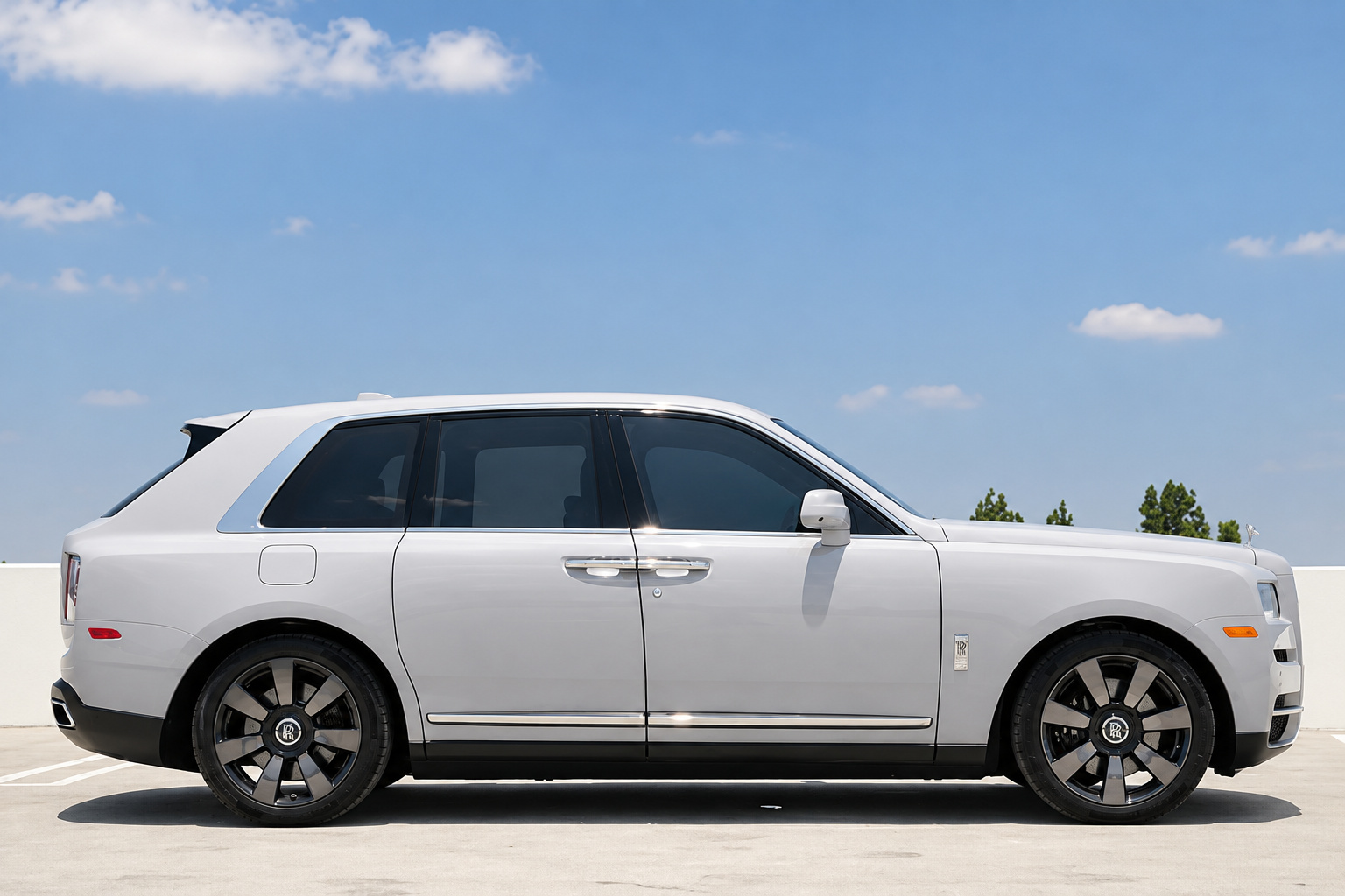 Side profile of the white Rolls Royce Cullinan on silver and black two-tone wheels, parked on a rooftop deck