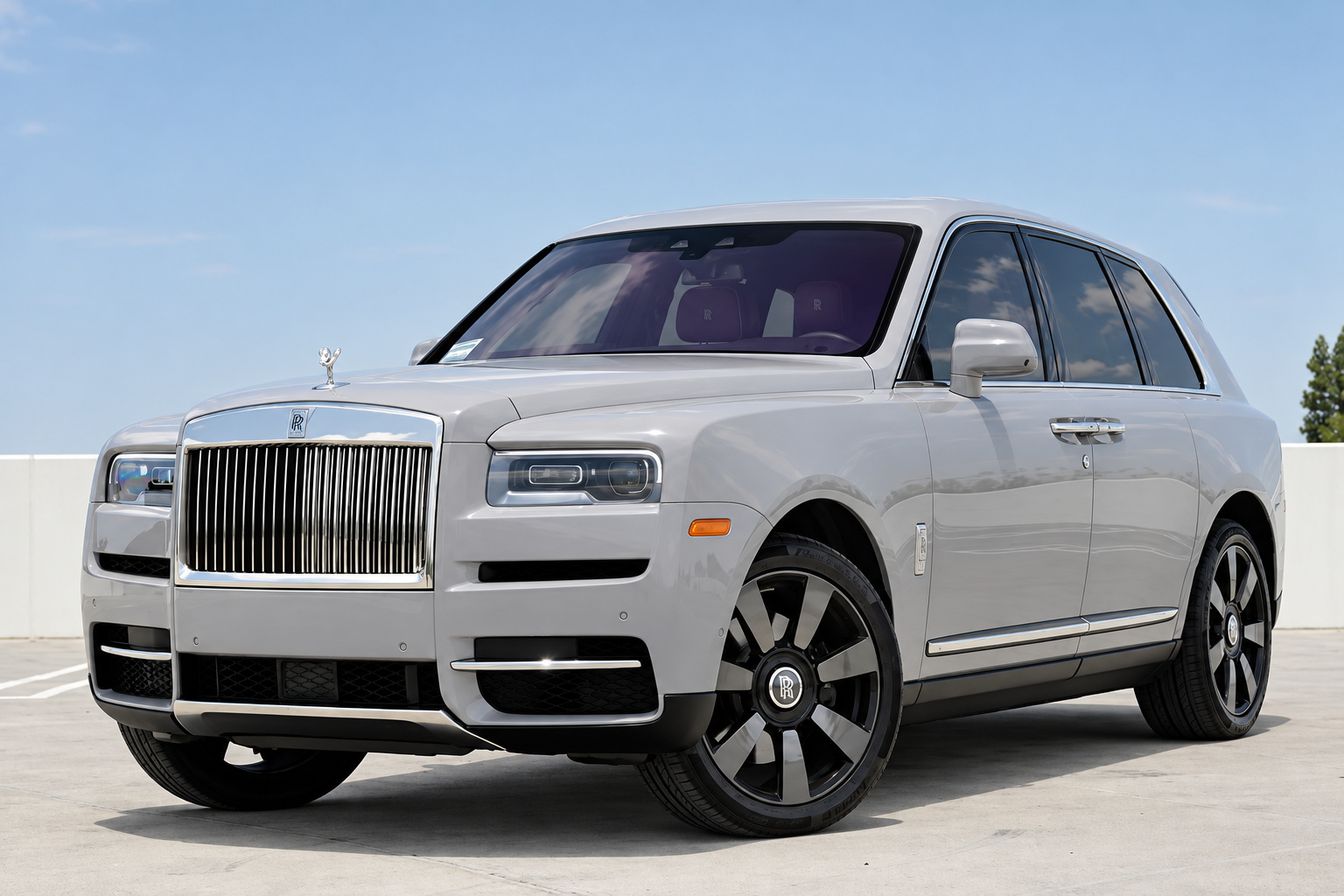 Front three-quarter view of the white Rolls Royce Cullinan with chrome grille and two-tone wheels under a clear sky