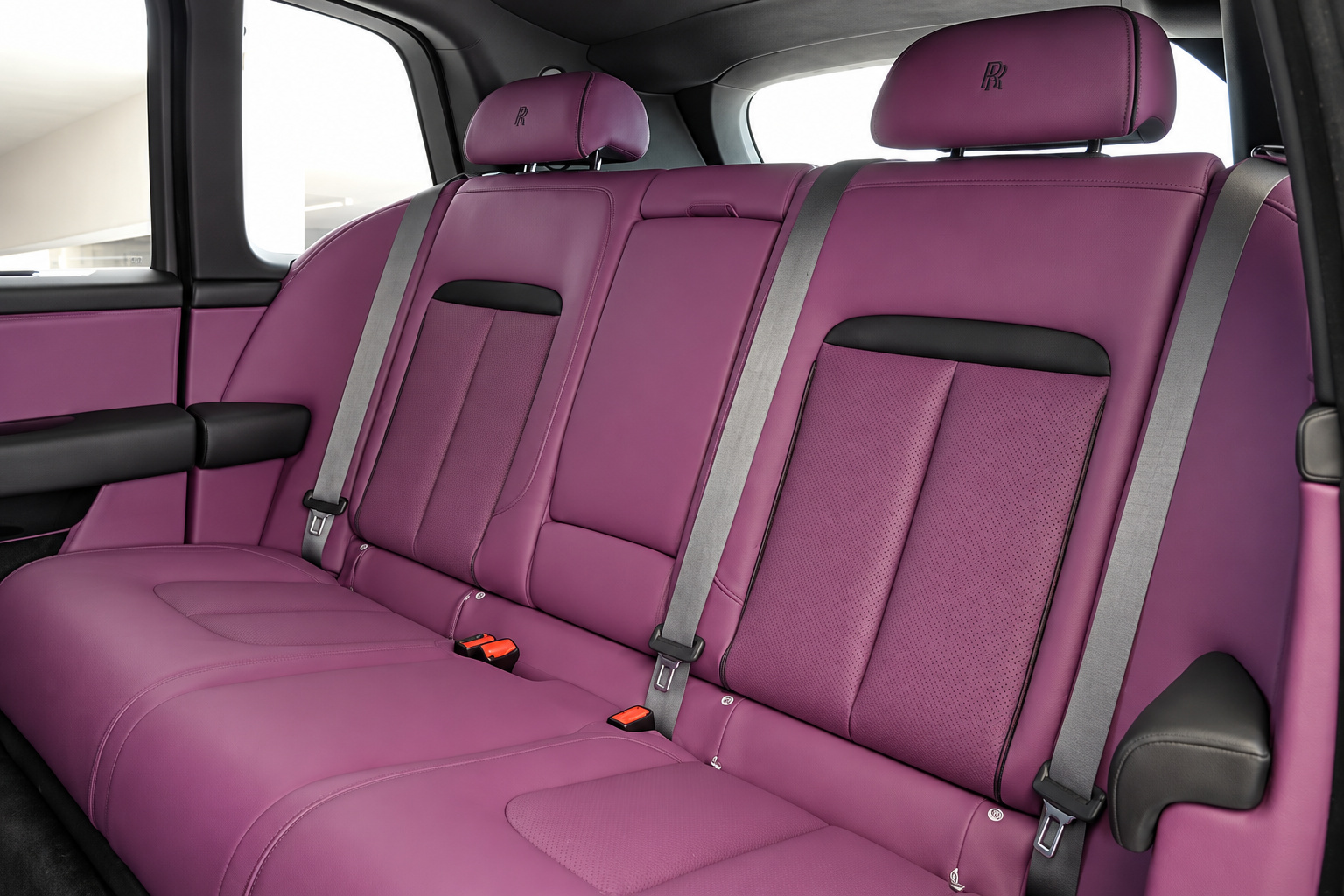 Rear bench of the white Cullinan in purple leather with black seatbelts and the white door frame behind