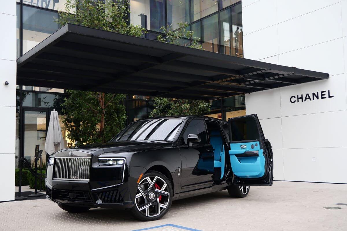 Black Rolls Royce Cullinan Black Badge Series II under a Rodeo Drive storefront canopy, rear door open on turquoise leather