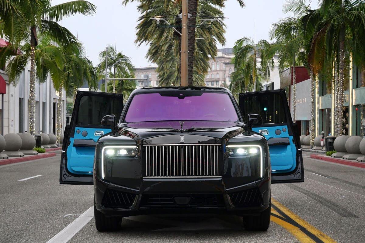 Black Cullinan Black Badge Series II head-on in the middle of Rodeo Drive with both front doors open and the grille lit