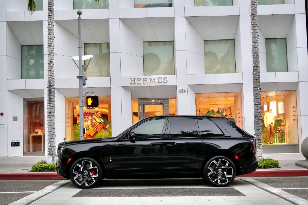 Side profile of the black Cullinan Black Badge Series II parked outside a Rodeo Drive flagship under palm trees