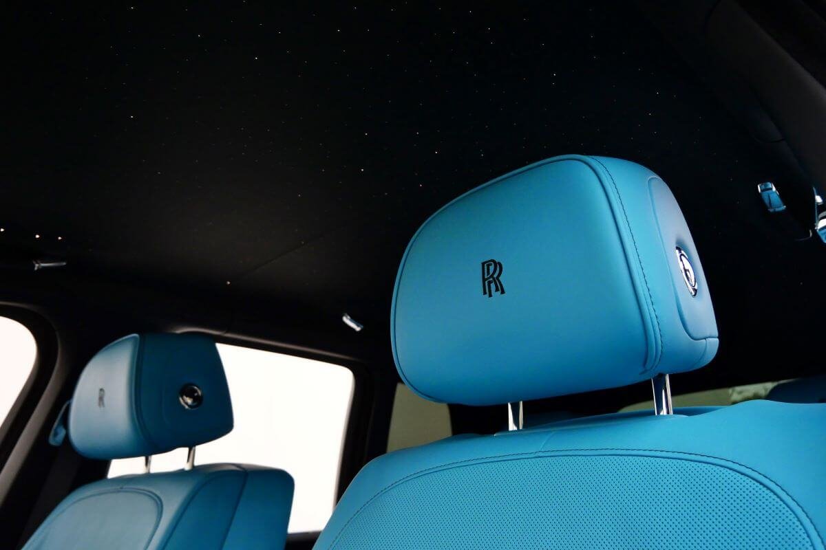 Turquoise rear headrest with embroidered RR monogram beneath the starlight headliner of the Black Badge Cullinan