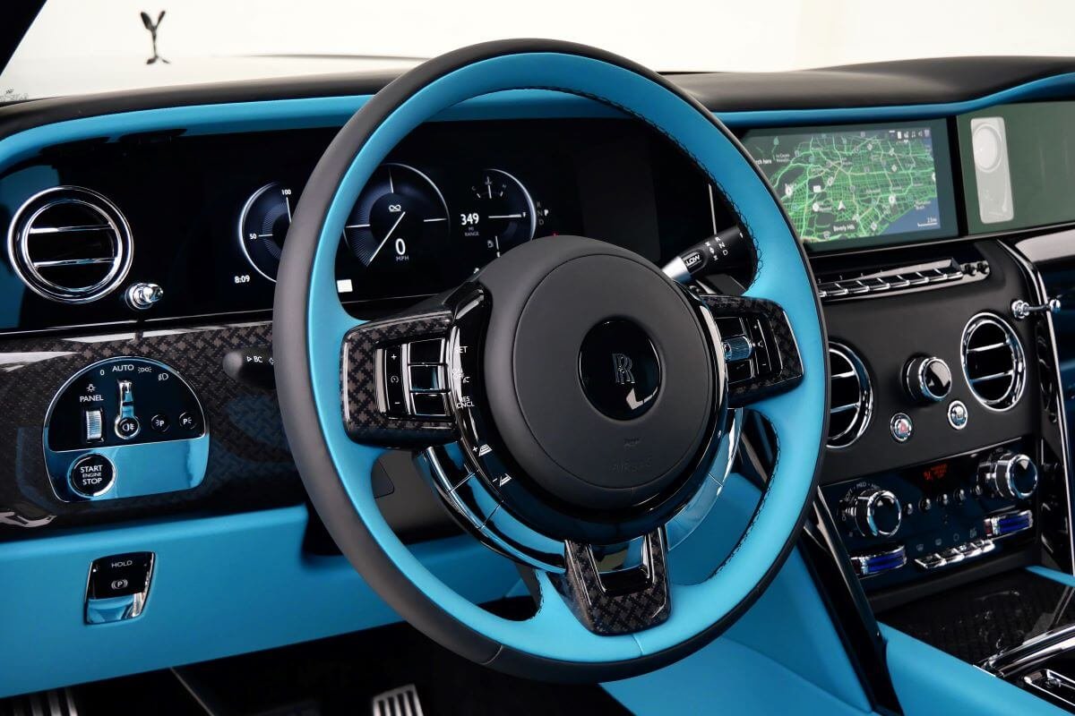 Turquoise and black steering wheel with carbon fibre trim and the digital gauge display in the Black Badge Cullinan