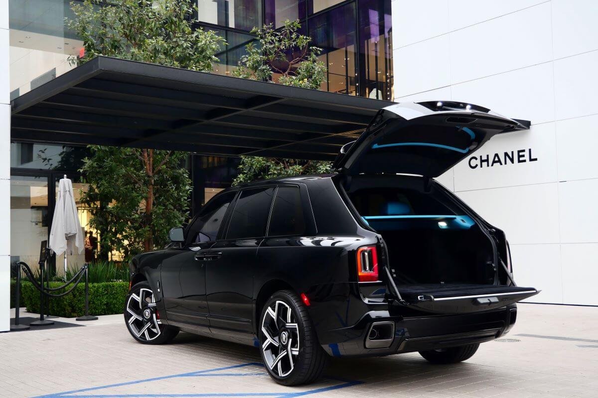 Rear three-quarter view of the black Cullinan Black Badge Series II with the powered tailgate open under a Rodeo Drive canopy