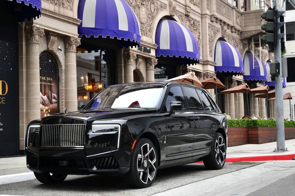 Black Rolls Royce Cullinan Black Badge Series II at the curb beneath striped awnings on Rodeo Drive in Beverly Hills