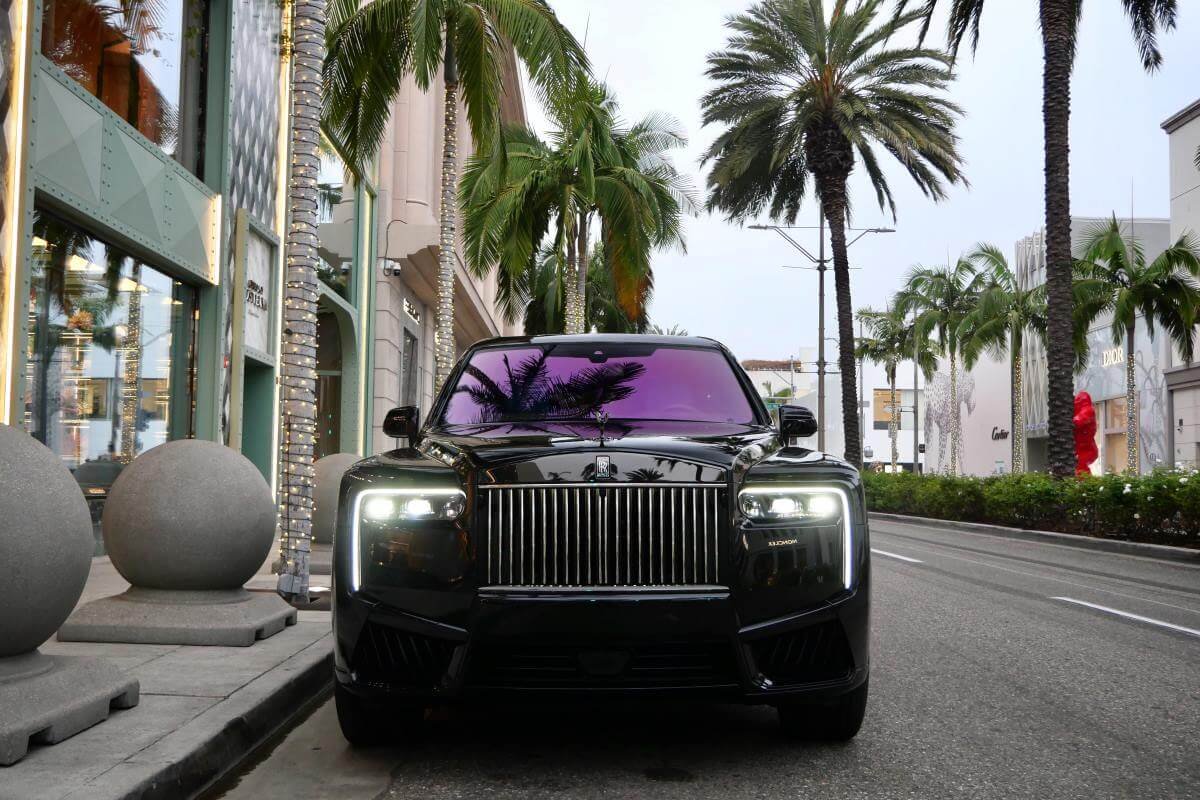 Black Cullinan Black Badge Series II head-on at the Rodeo Drive curb with the grille and headlights lit, palms behind
