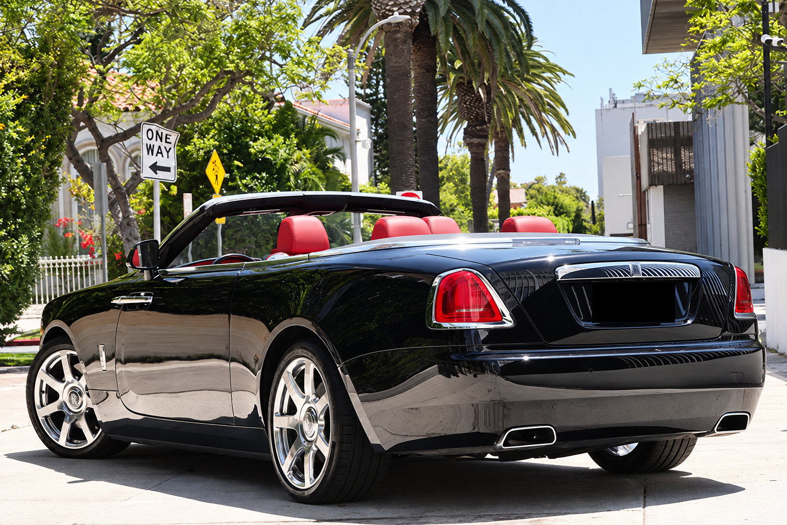 Rear three-quarter view of the black Rolls Royce Dawn convertible, roof stowed, red headrests above the wood deck