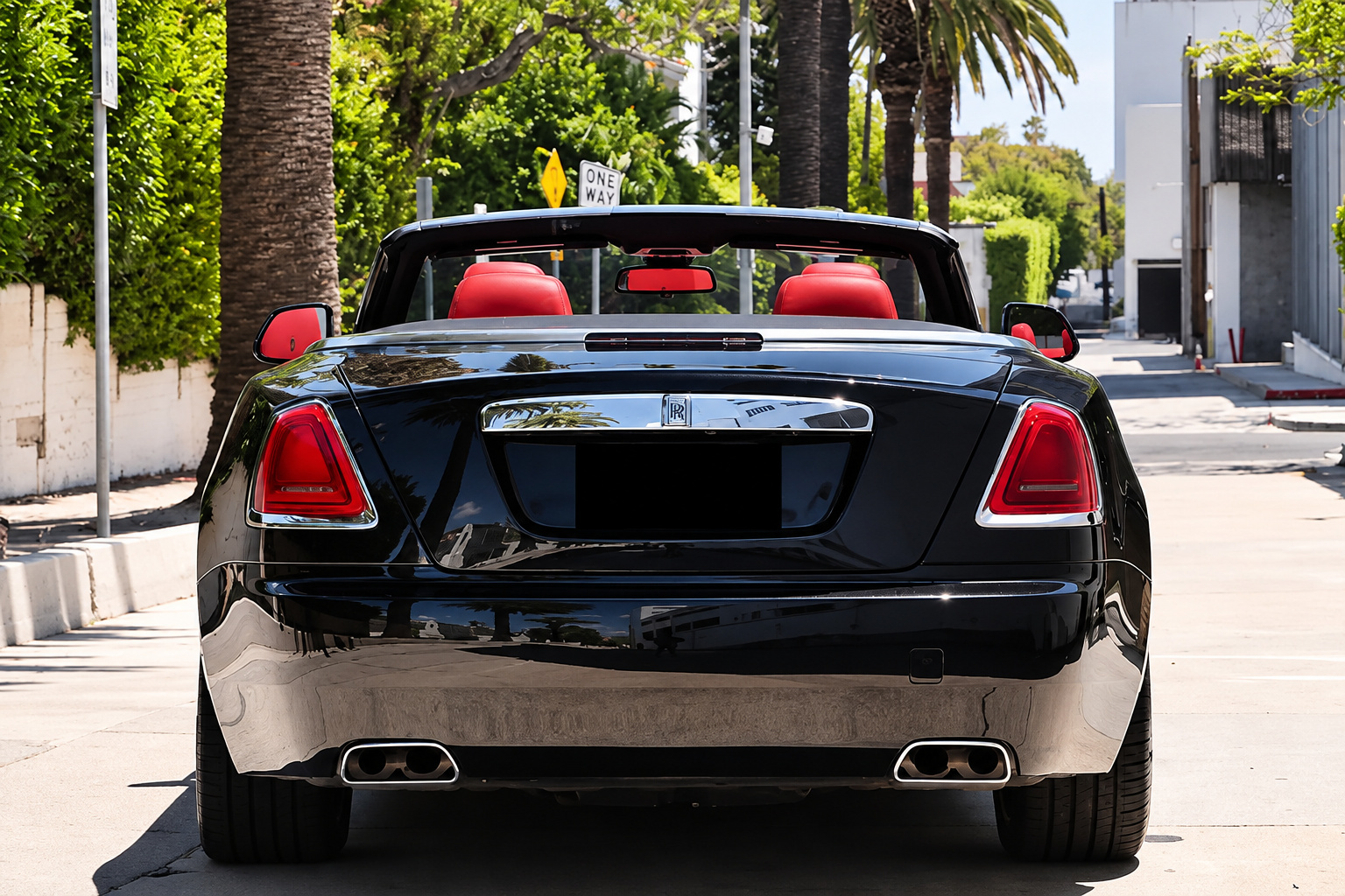 Black Rolls Royce Dawn from behind with the roof down, 4 red seats visible and twin exhaust tips below