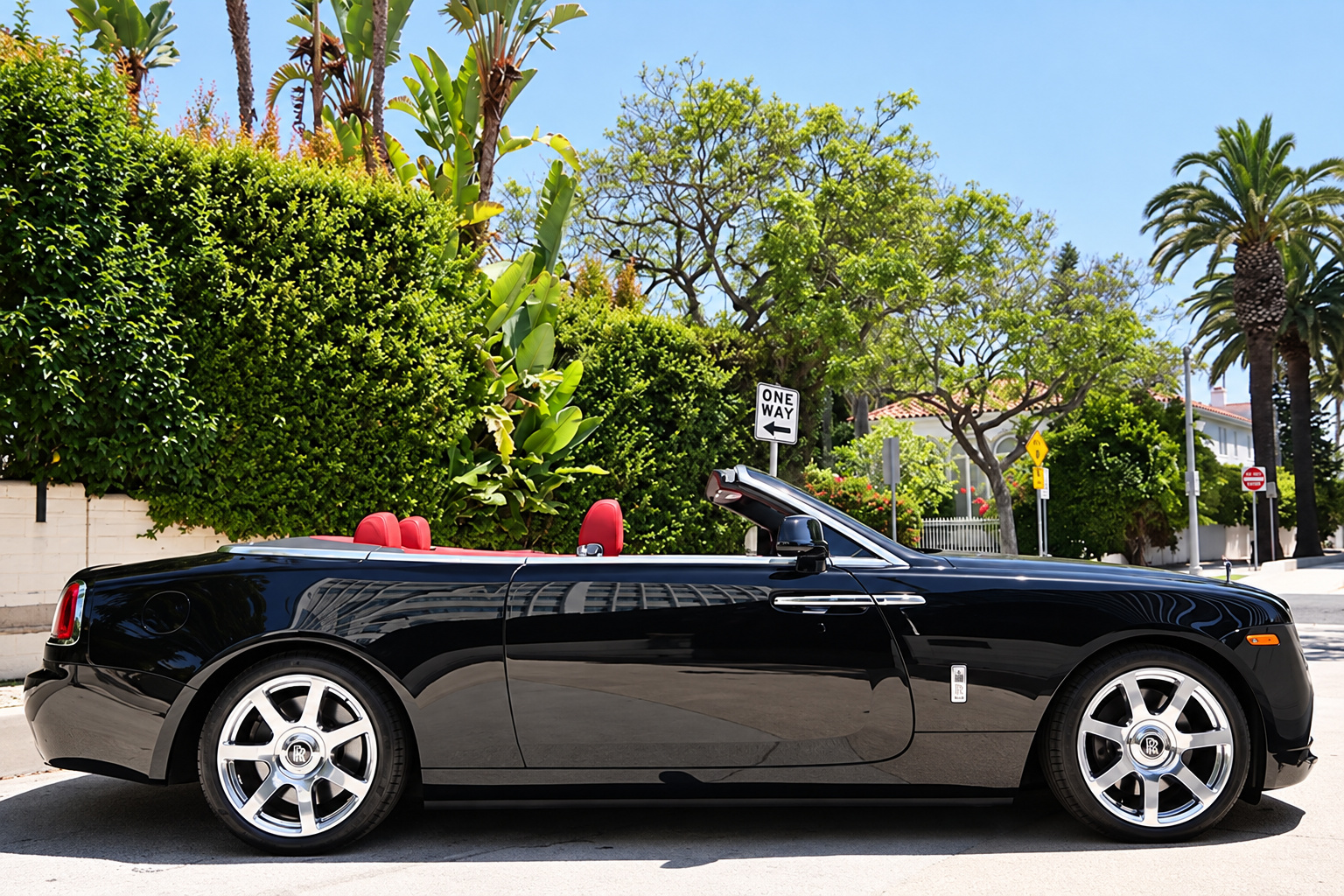 Side profile of the black Rolls Royce Dawn with the top down on chrome 21-inch wheels under the palms