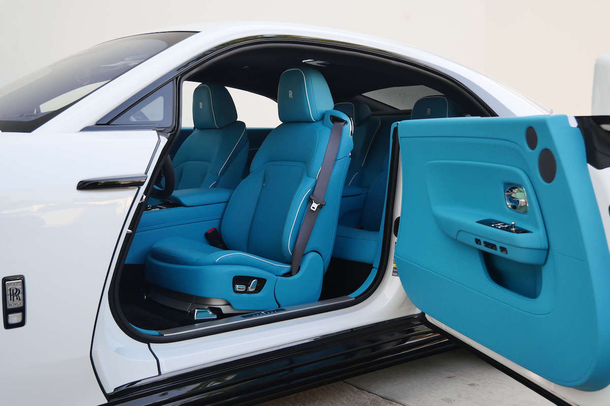 The wide coach door of the white Spectre open on the turquoise front seat and door panel