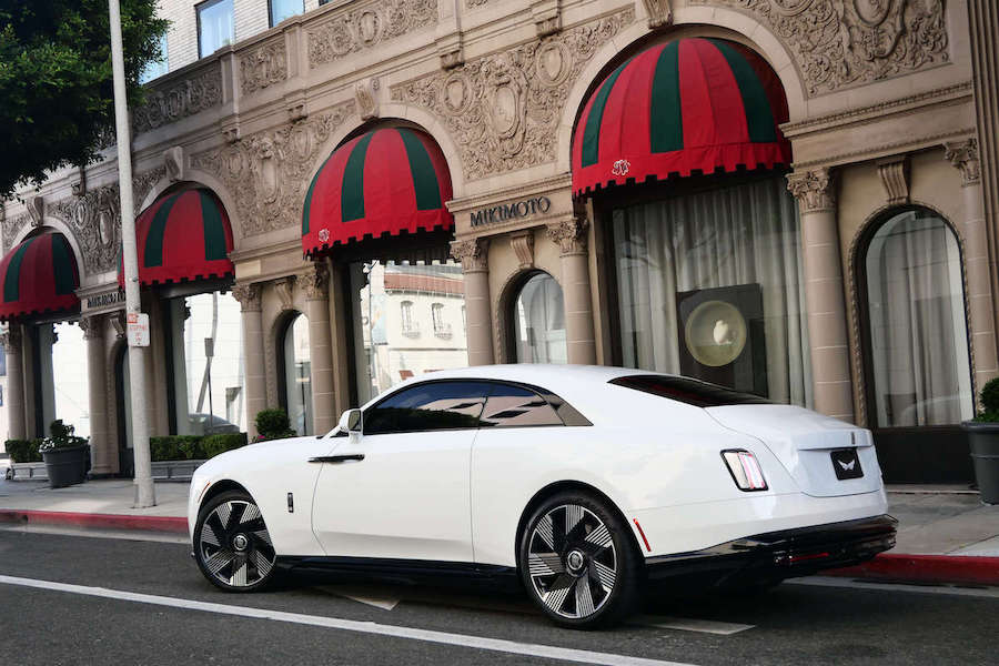 Rear three-quarter view of the white Spectre at the curb beneath red awnings on Rodeo Drive