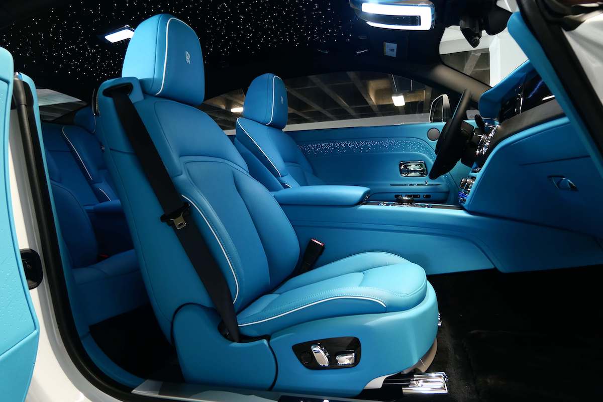 Driver's seat of the white Spectre in turquoise leather with the coach door open and the starlight headliner above