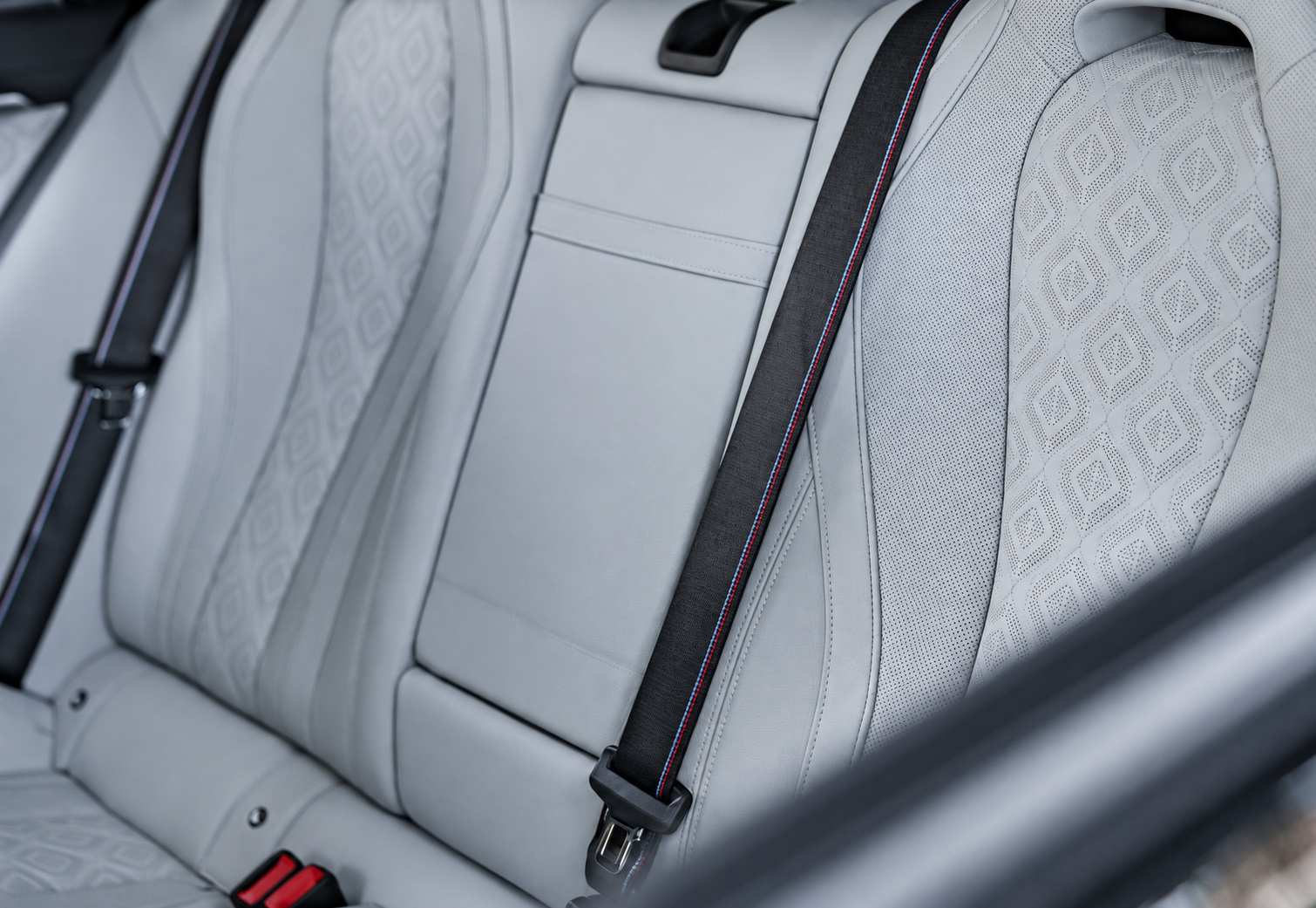 Ivory white quilted rear seat of the M8 Competition Gran Coupe with the M-striped seat belt