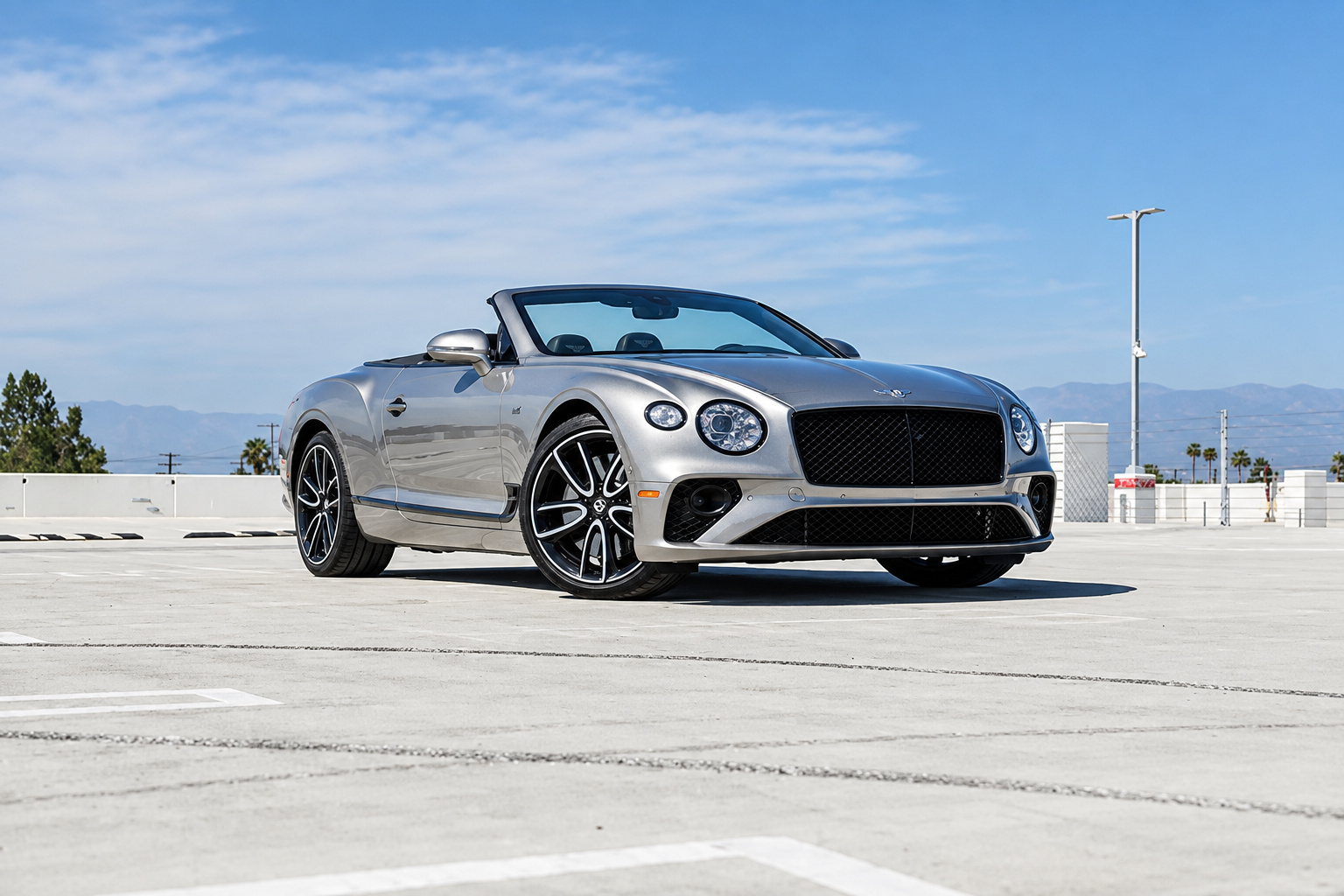 Light silver Bentley Continental GTC First Edition roof down, front three-quarter on a rooftop deck with mountains behind