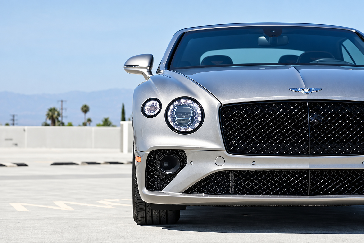 Front detail of the silver Continental GTC, crystal-cut headlight and the chrome mesh grille in direct sun