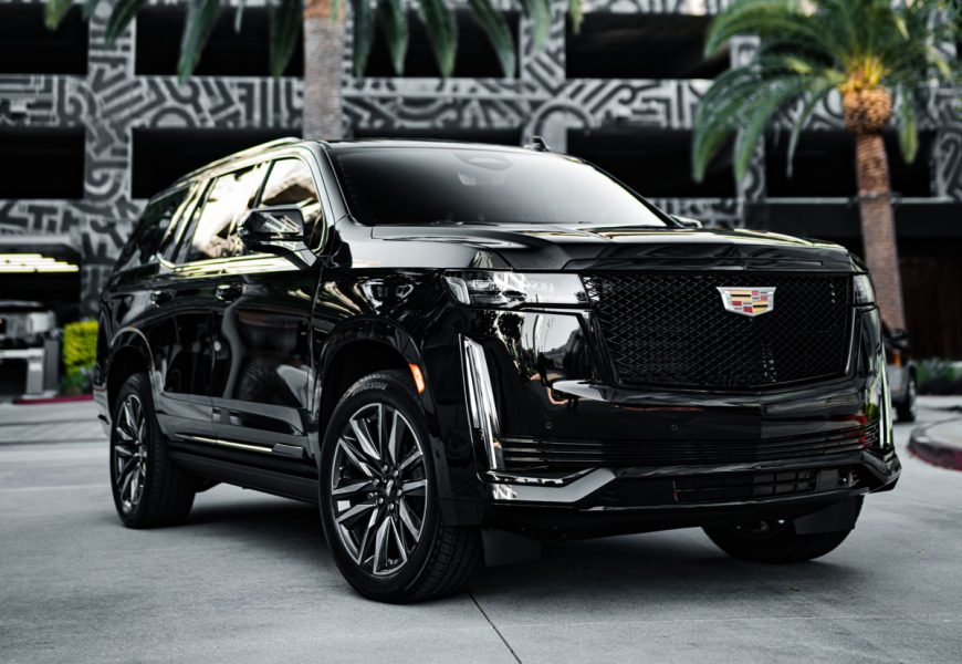 Black Cadillac Escalade Sport Platinum front three-quarter on a city street with a patterned wall and palms