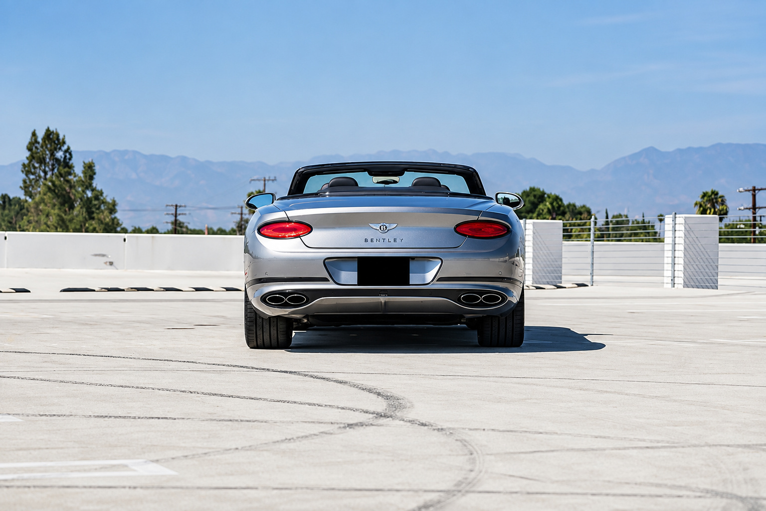 Rear view of the silver Bentley Continental GTC First Edition, roof folded, on a rooftop deck with mountains