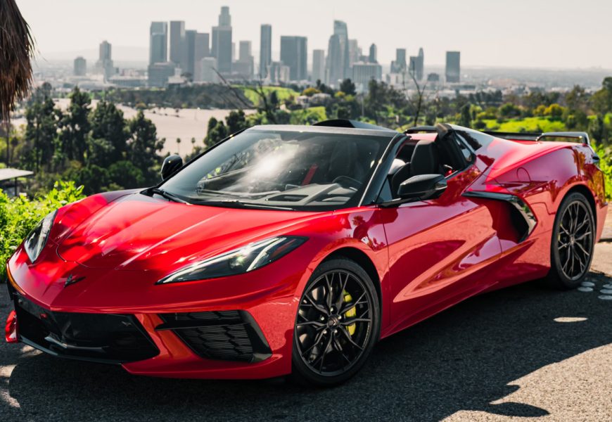 Red Chevrolet Corvette C8 Stingray with the roof panel off, front three-quarter at an overlook above downtown Los Angeles