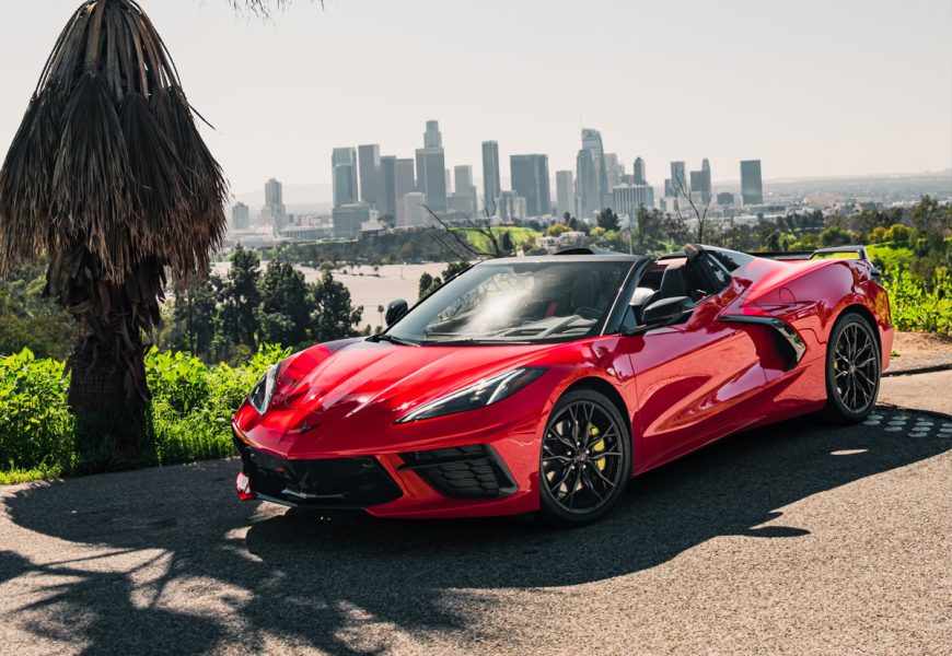 Red Corvette C8 Stingray from a low front angle beside a palm tree with downtown Los Angeles in the distance