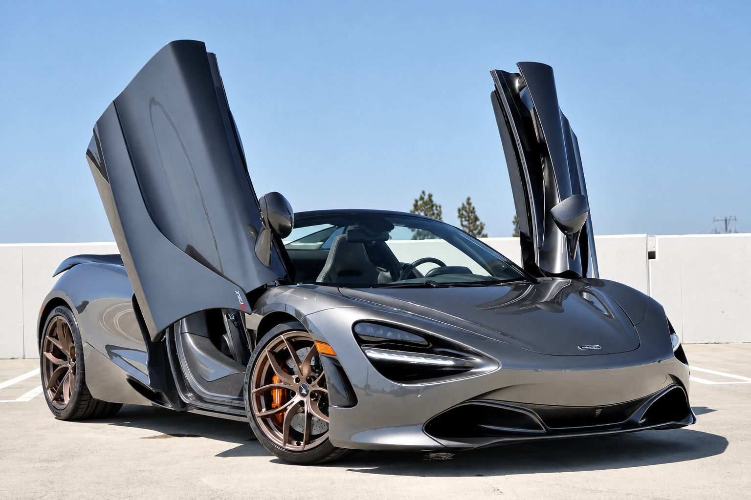 Dark grey McLaren 720S Spider with both dihedral doors up and the roof down on a rooftop parking deck in Los Angeles