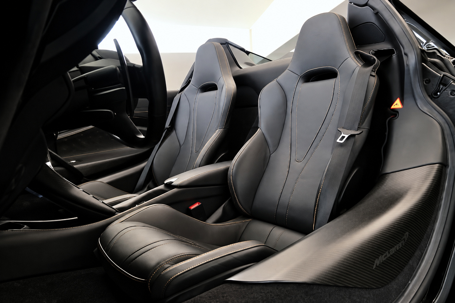 Black leather seats with orange contrast stitching in the McLaren 720S Spider, shot from the open passenger door