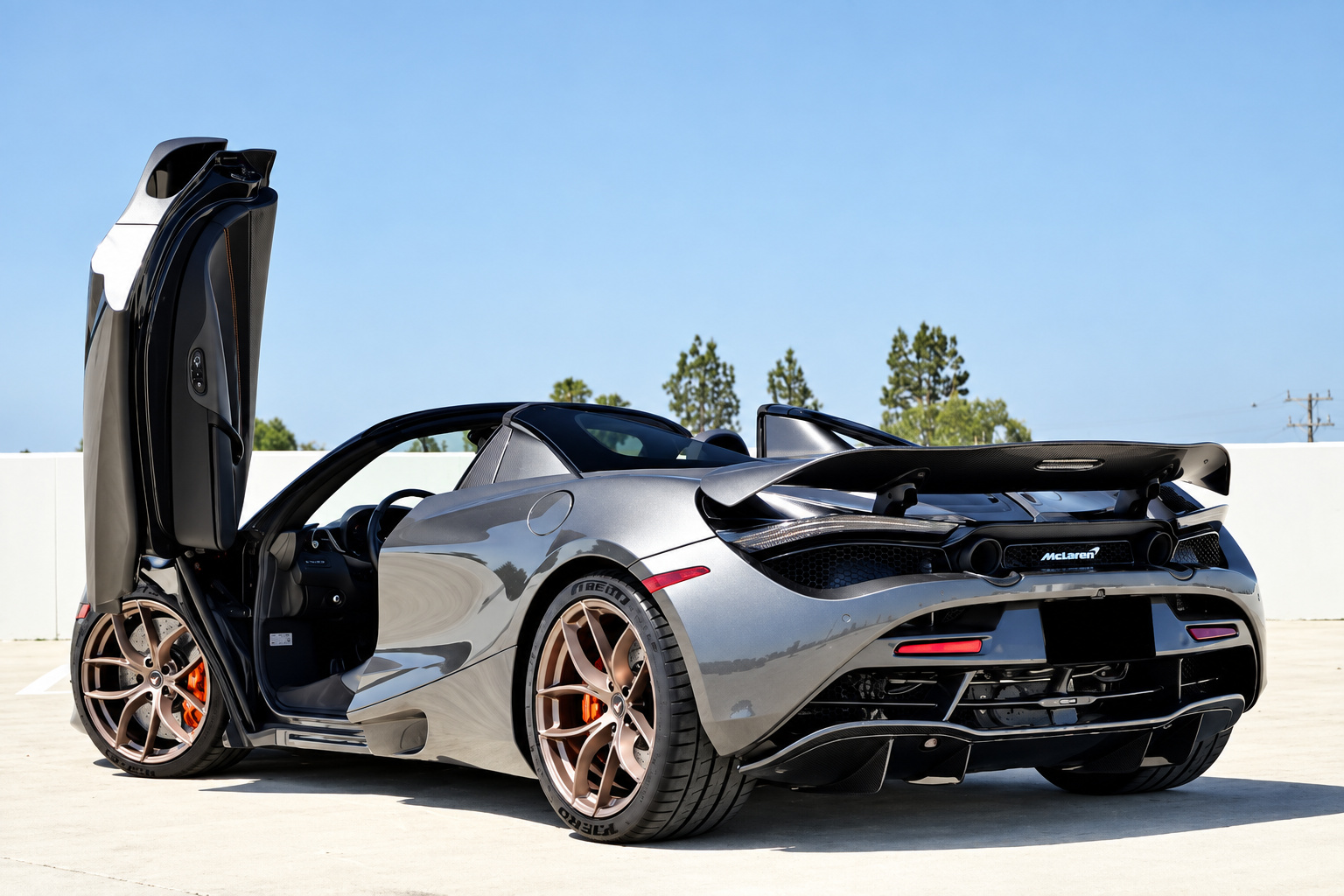 Rear three-quarter of the dark grey McLaren 720S Spider, driver door up, roof down, bronze wheels and orange calipers