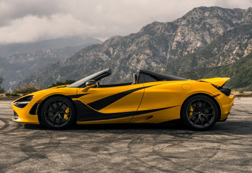 Side profile of the yellow 720S Spider MSO, roof down, black stripe running the length of the car, San Gabriels behind