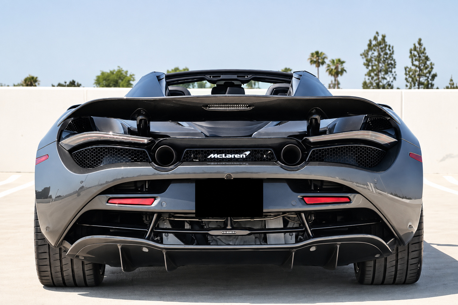 Straight-on rear view of the grey McLaren 720S Spider with the roof down, twin exhausts and the full-width airbrake