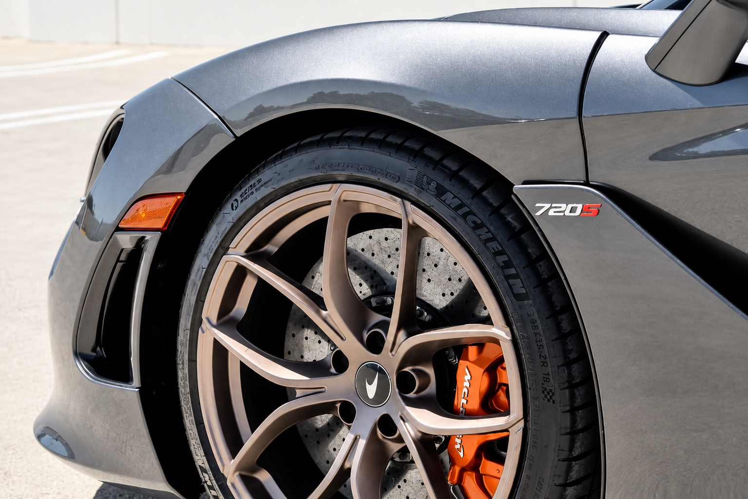 Front wheel of the 720S Spider close up, bronze-finish wheel, orange caliper and the 720S badge on the grey fender