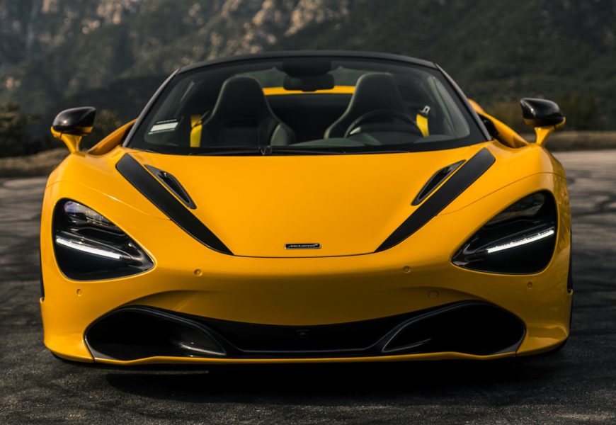 Head-on view of the yellow 720S Spider MSO, black stripes over the hood and the mountain ridgeline behind