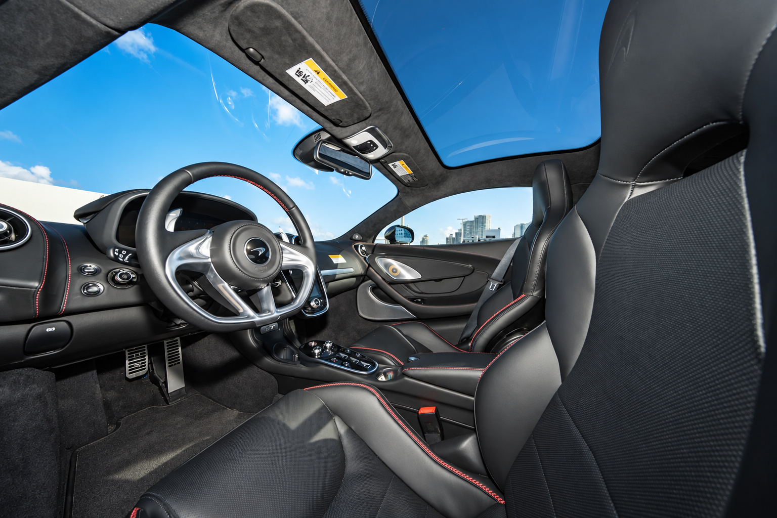 Black leather cabin of the McLaren GT with red contrast stitching, steering wheel and seats from the open door