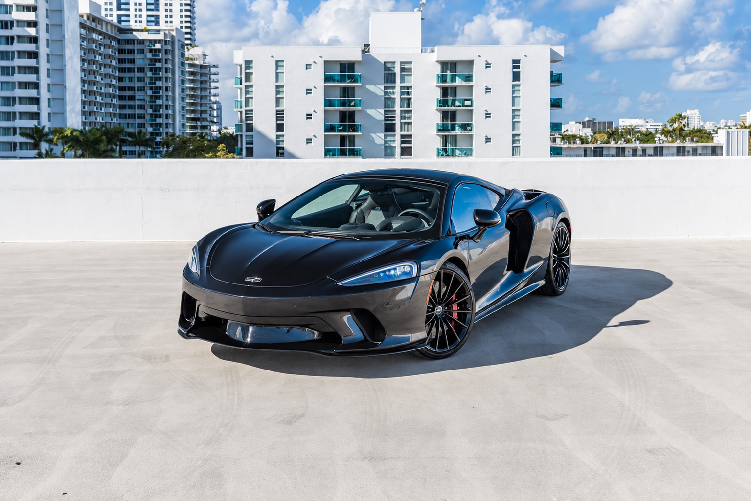 Front three-quarter of the black metallic McLaren GT parked on a rooftop deck, black multi-spoke wheels