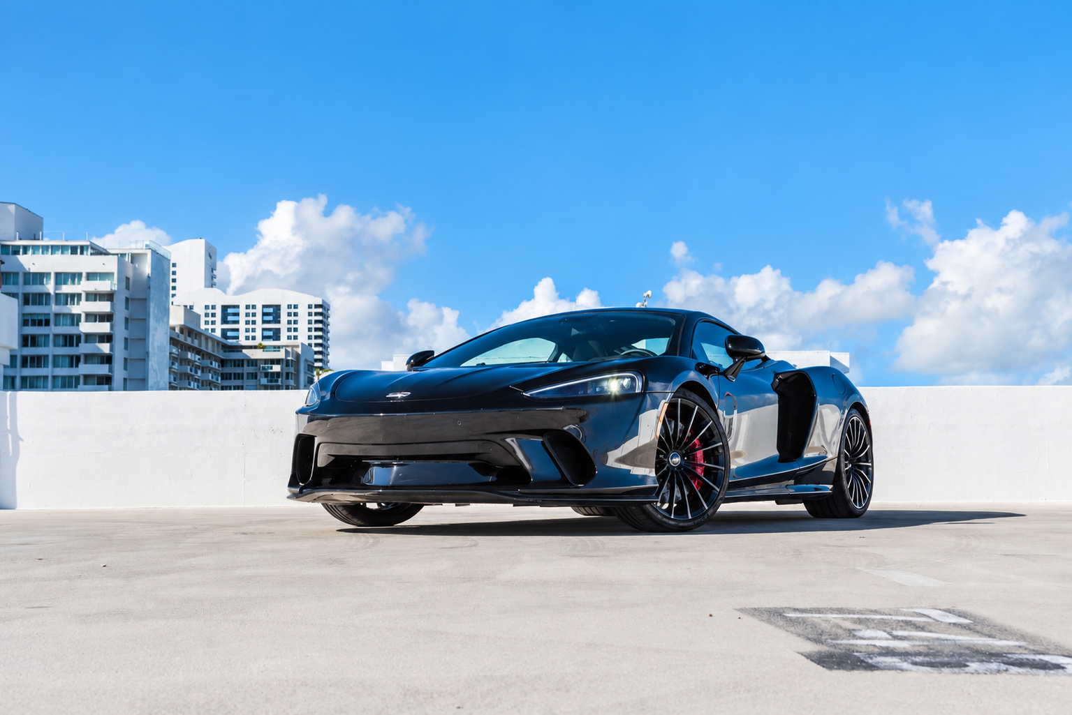 Front three-quarter of the black McLaren GT from the driver's side, low nose and long tail under a clear sky