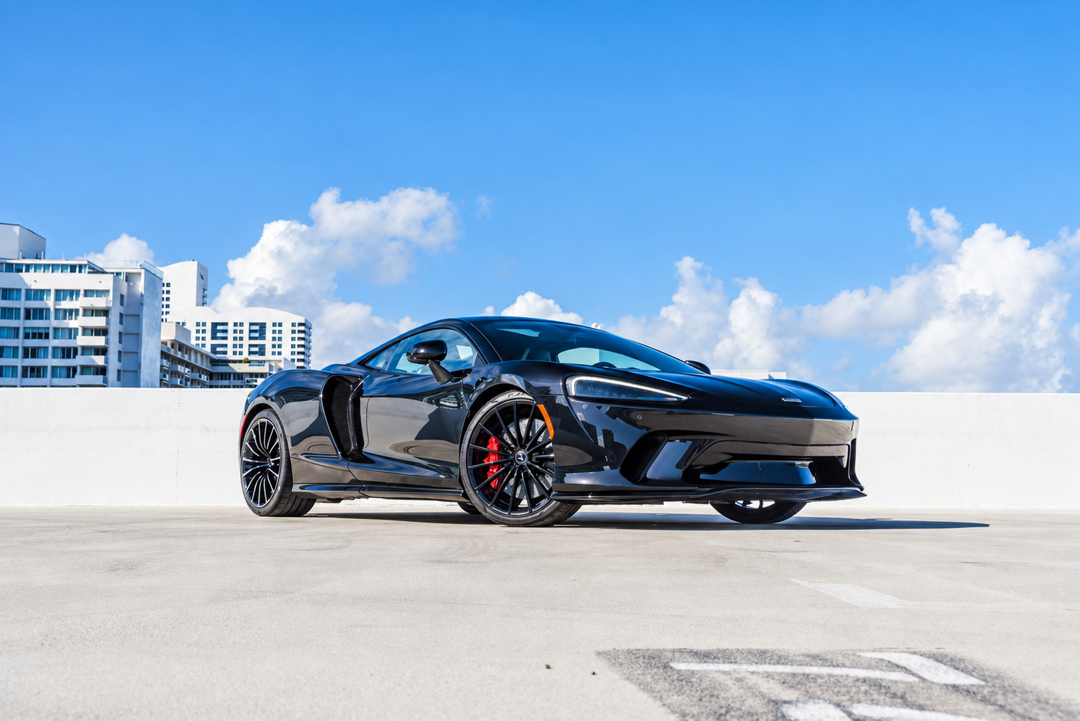 Side-on view of the black metallic McLaren GT, doors closed, showing the long glass tailgate and rear deck