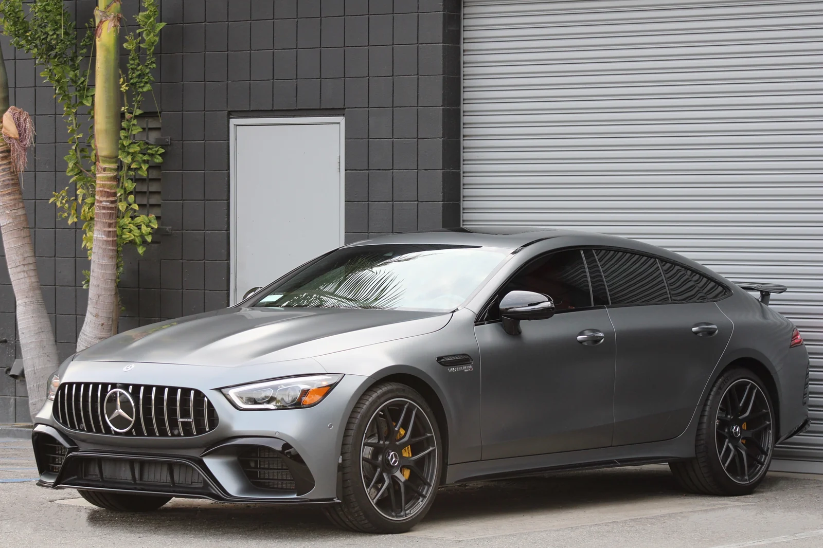 Satin grey Mercedes-AMG GT 63 four-door, front three-quarter view with black wheels and the vertical-bar AMG grille