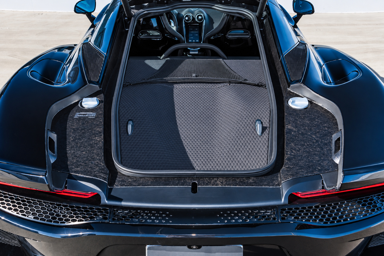 Rear luggage bay of the McLaren GT with the glass tailgate open, carpeted floor and tie-down loops from above