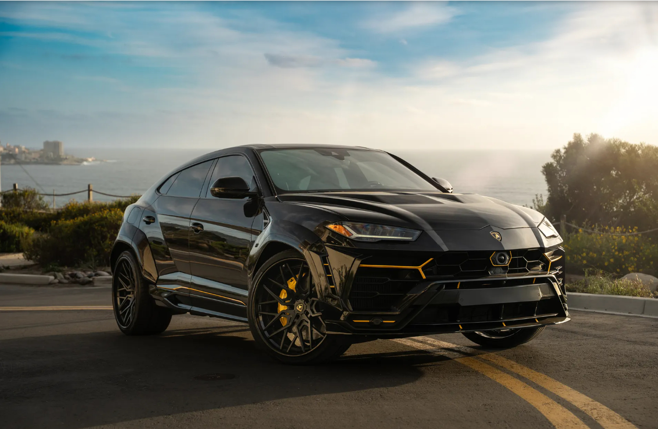 Black Lamborghini Urus Widebody front three-quarter on a coast road above the ocean, yellow calipers and black wheels