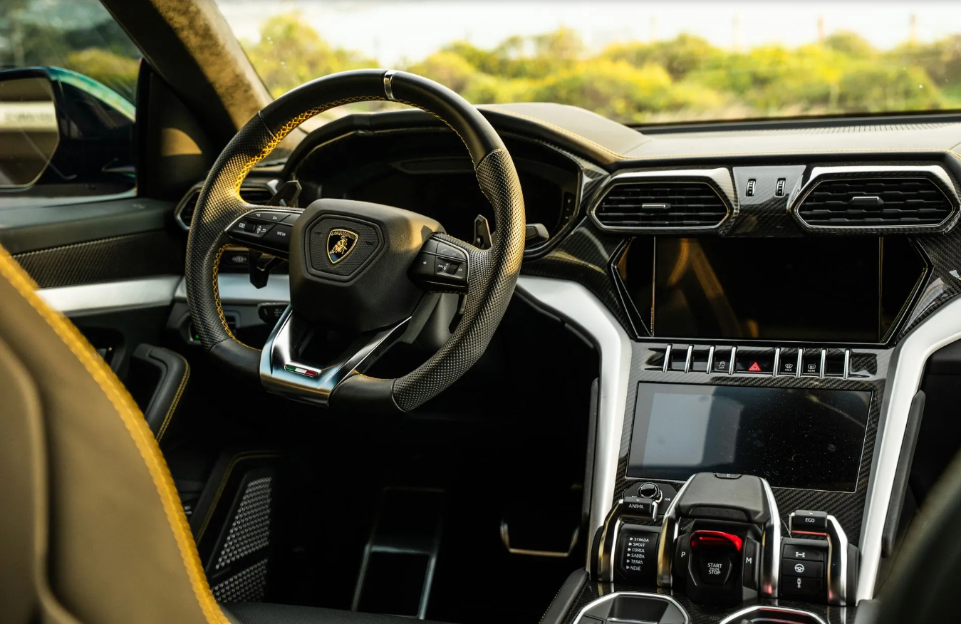 Driver's view of the Urus Widebody cabin, yellow-stitched wheel, carbon dash trim and the tamburo drive selector