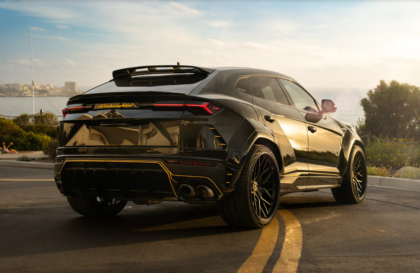 Rear three-quarter of the black Lamborghini Urus Widebody on a cliff road at sunset, flared arches and quad exhaust