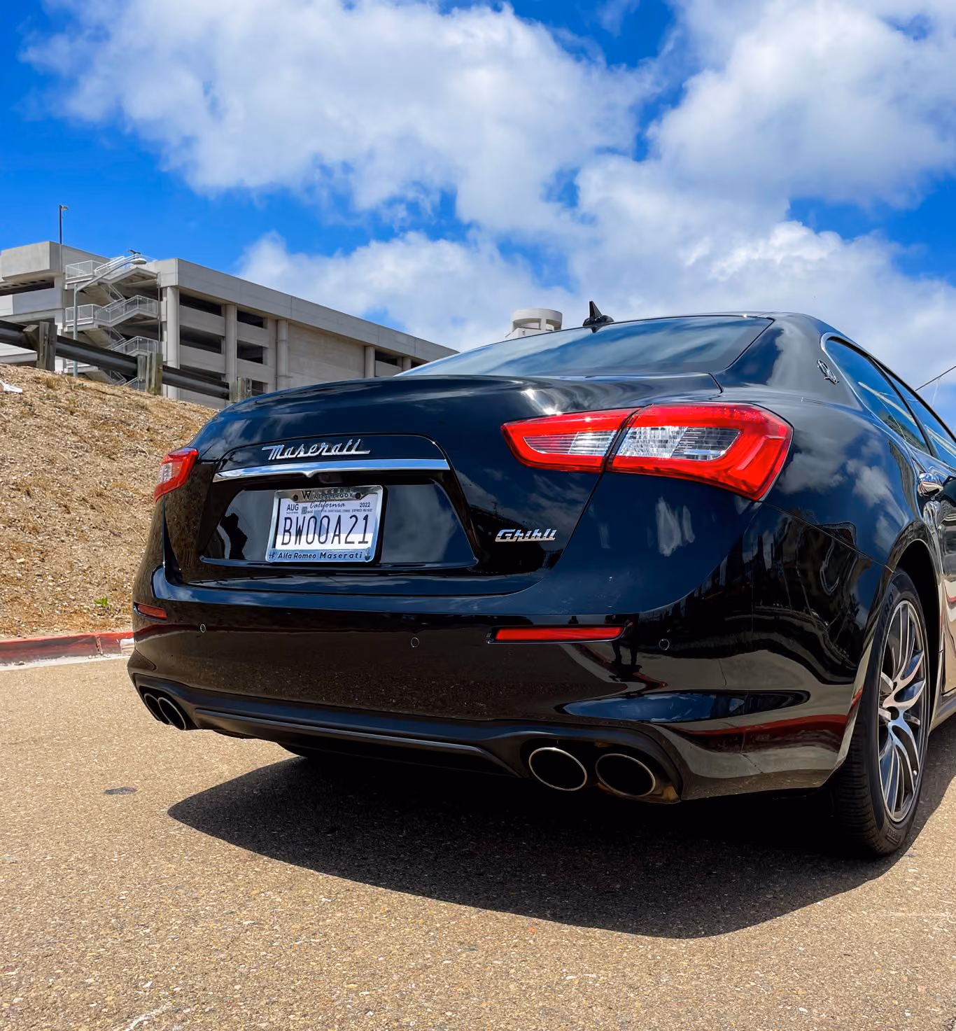 Rear three-quarter of the black Maserati Ghibli showing the quad exhaust tips, low angle against a blue sky