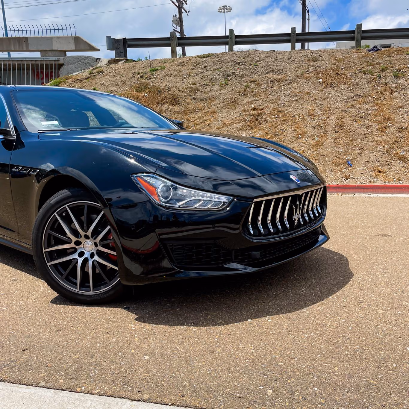 Low front three-quarter of the black Maserati Ghibli, trident grille and silver multi-spoke wheel up close