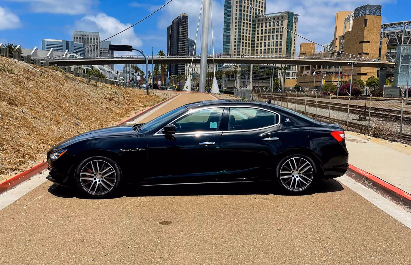 Side profile of the black Maserati Ghibli on silver wheels, downtown towers in the background