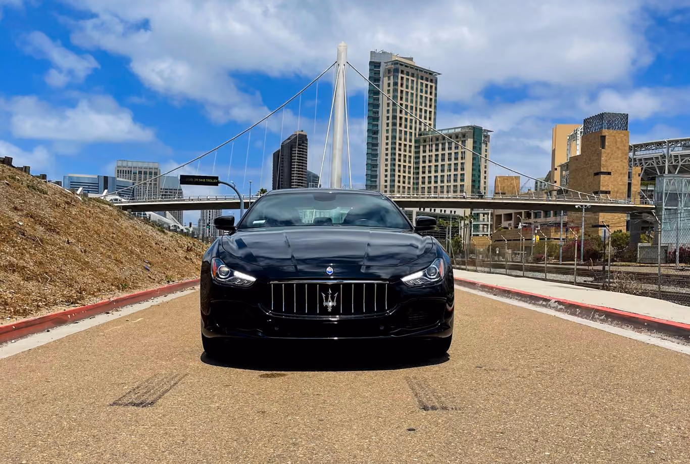 Head-on view of the black Maserati Ghibli with a white bridge pylon and a city skyline behind