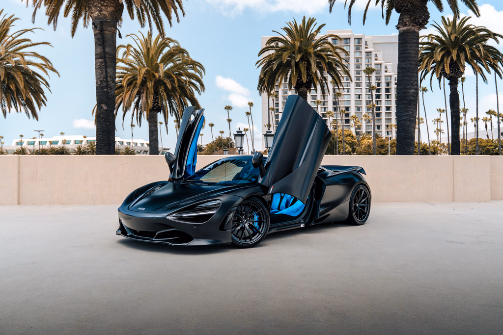 Satin black McLaren 720S Spider with both dihedral doors raised and the roof down on a palm-lined rooftop deck