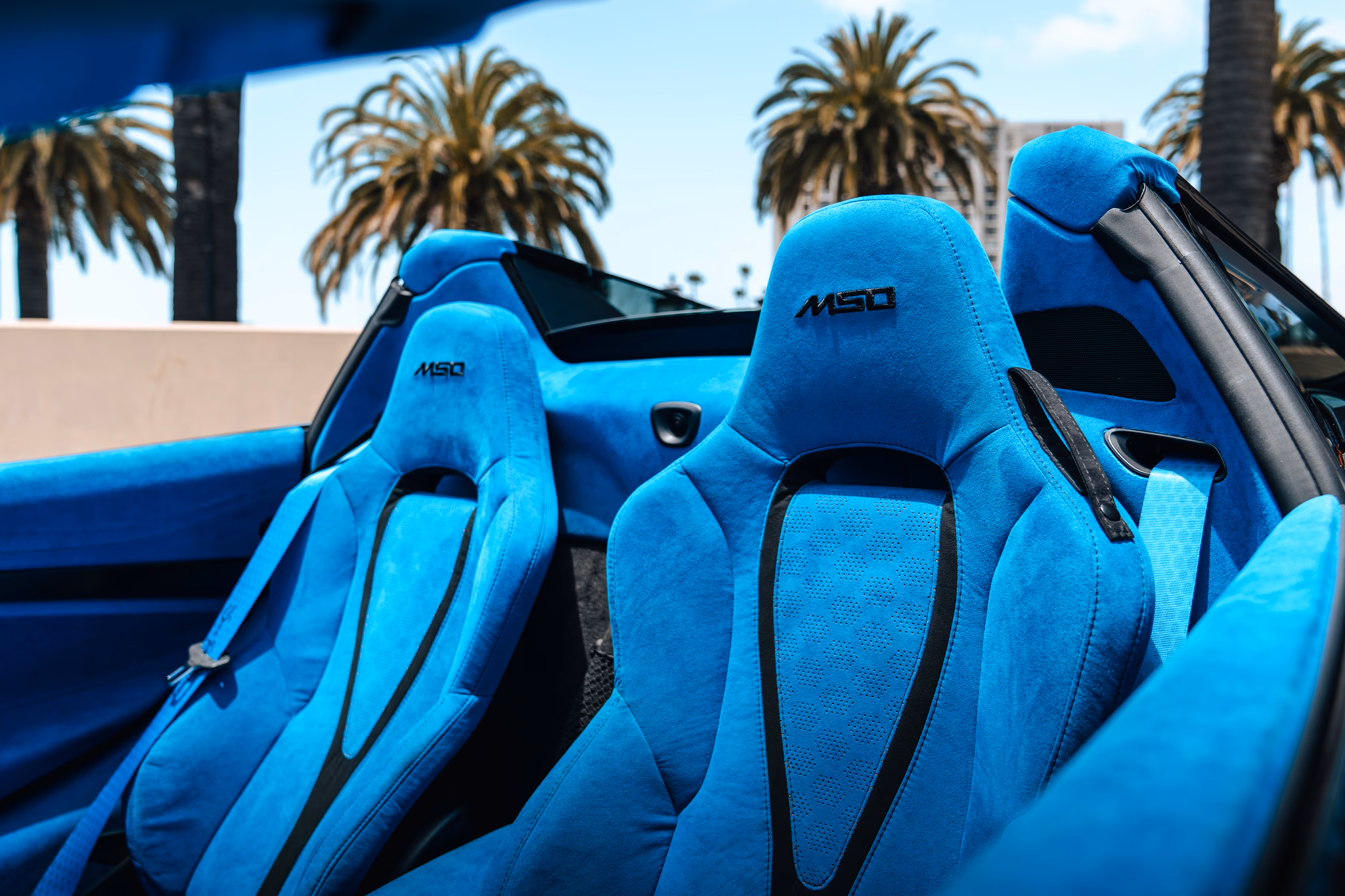 Bright blue MSO alcantara seats inside the McLaren 720S Spider, roof folded, palm trees behind the headrests