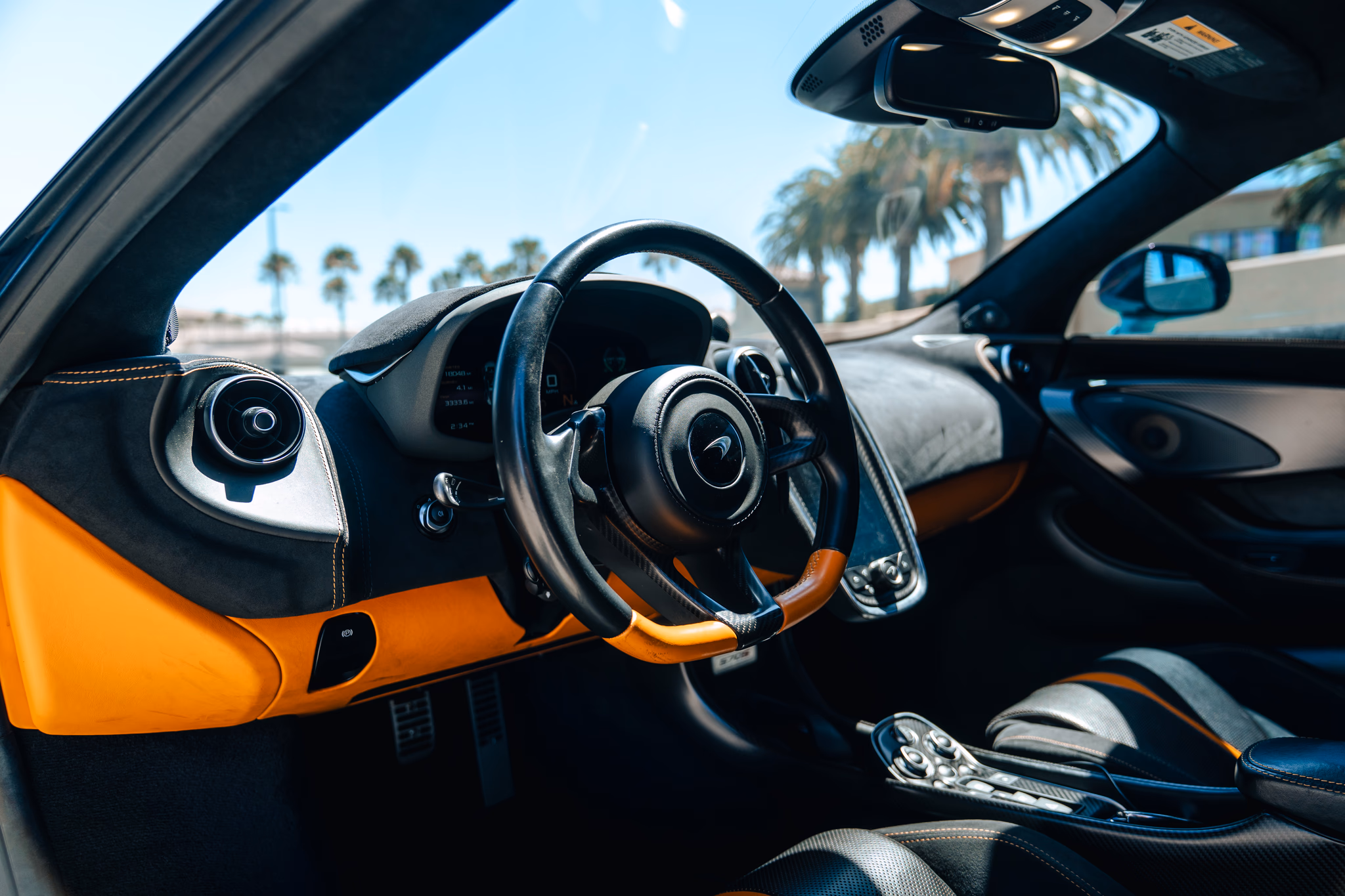 Driver's view of the 570S cabin, black steering wheel, orange leather door panel and the dash